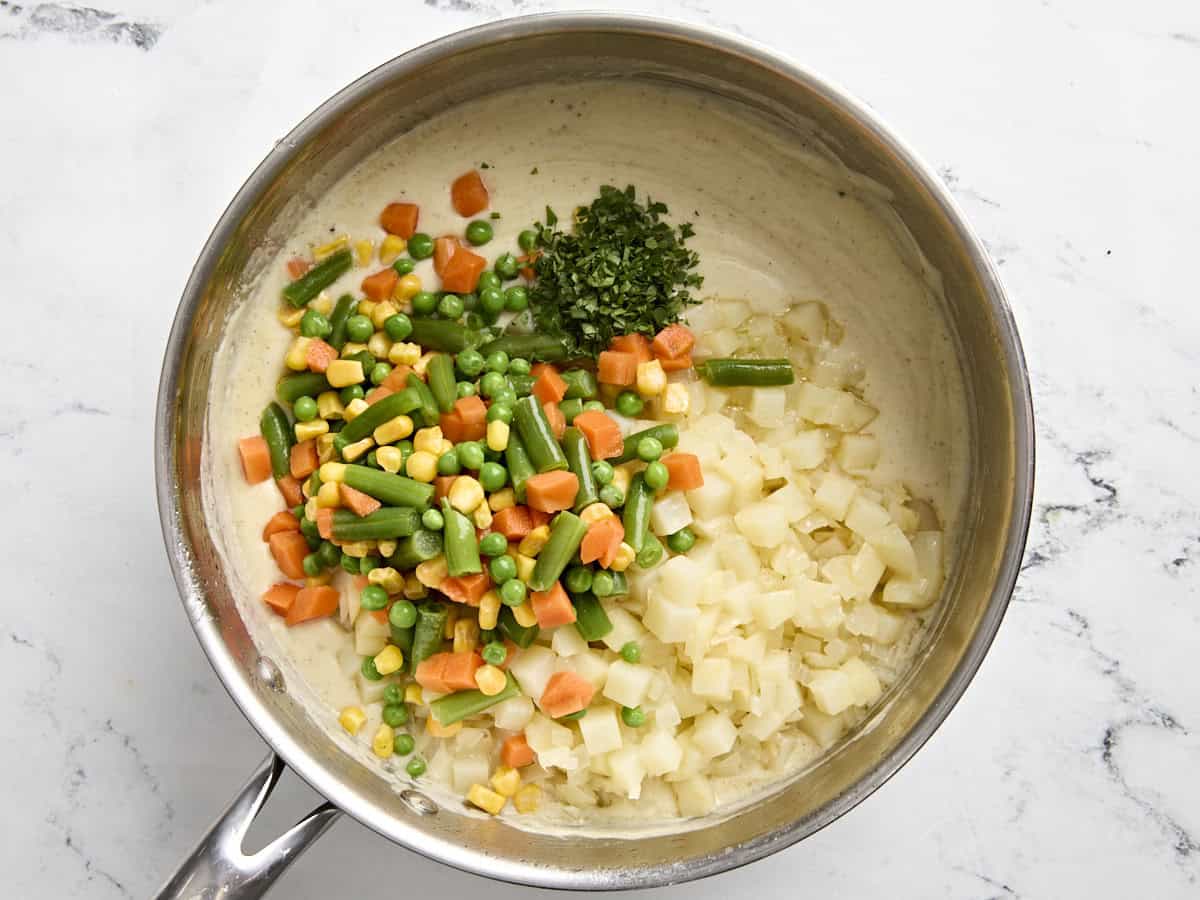 Diced potatoes and mixed vegetables added to the creamy sauce for turkey pot pie in a sauce pan.