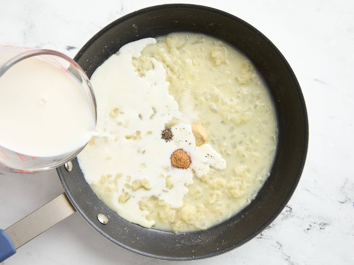 Milk being poured into a skillet with diced onions.