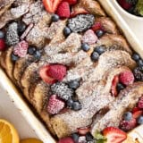 Overhead view of baked french toast with berries and powdered sugar in a casserole dish.