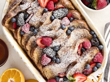 Overhead view of baked french toast with berries and powdered sugar in a casserole dish.