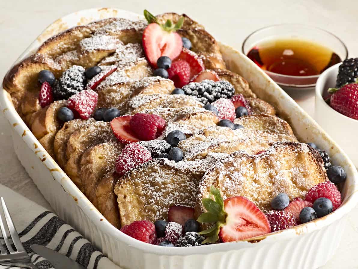 Side view of baked french toast, topped with powdered sugar and fresh berries in a casserole dish.