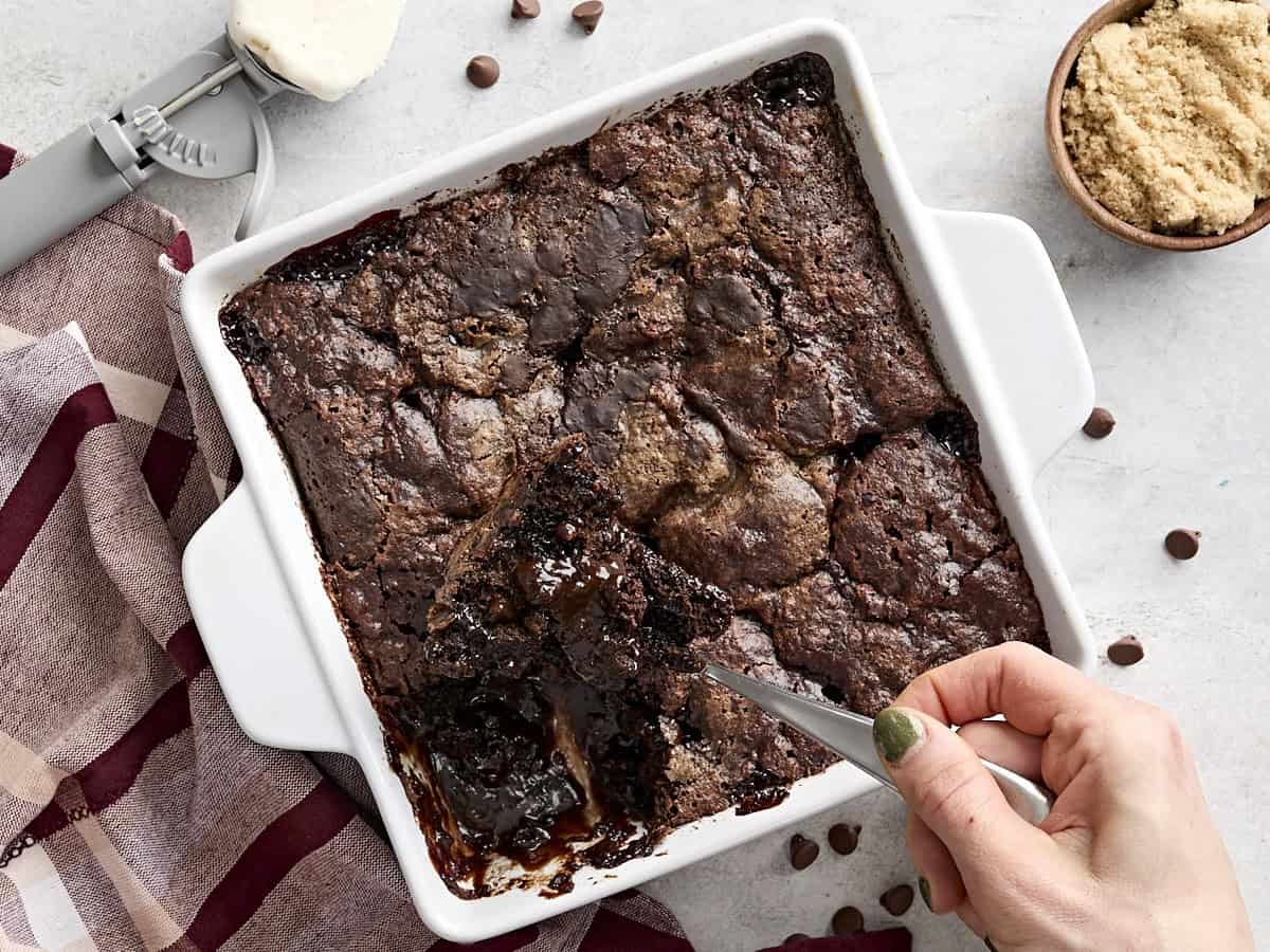 Overhead view of a spoon scooping some chocolate pudding cake out of a cake pan.