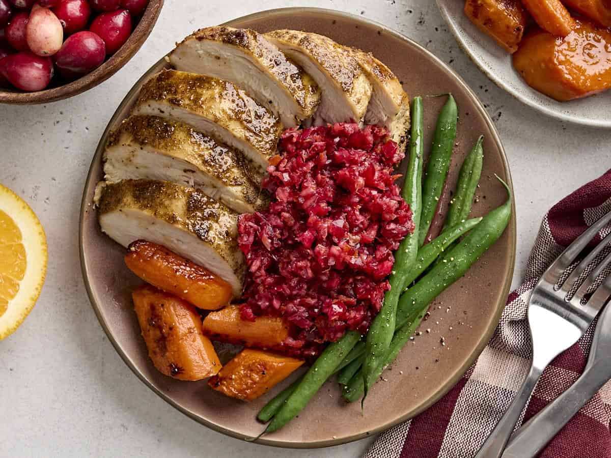 Overhead view of cranberry orange relish on a plate with sliced turkey, roasted carrots, and green beans.