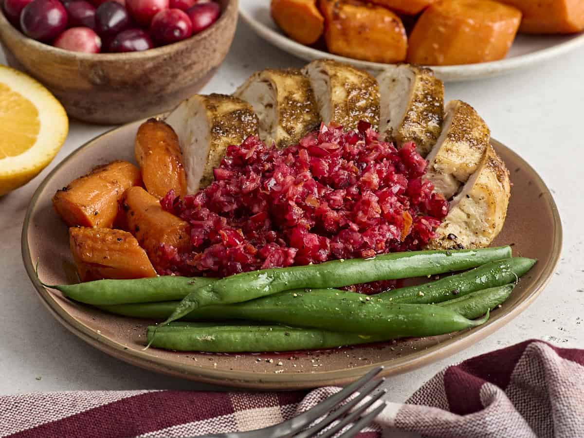 Side view of cranberry orange relish on a plate with sliced turkey, roasted carrots, and green beans.