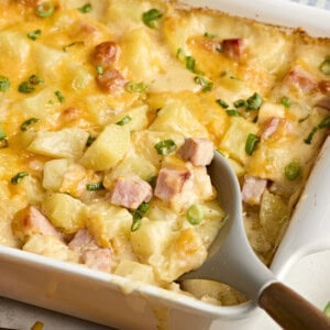 A serving spoon scooping ham and potato casserole from a baking dish.