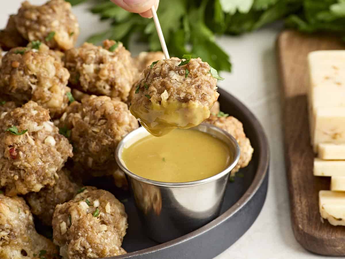 Side view of a sausage ball on a cocktail stick dipped in honey mustard sauce.