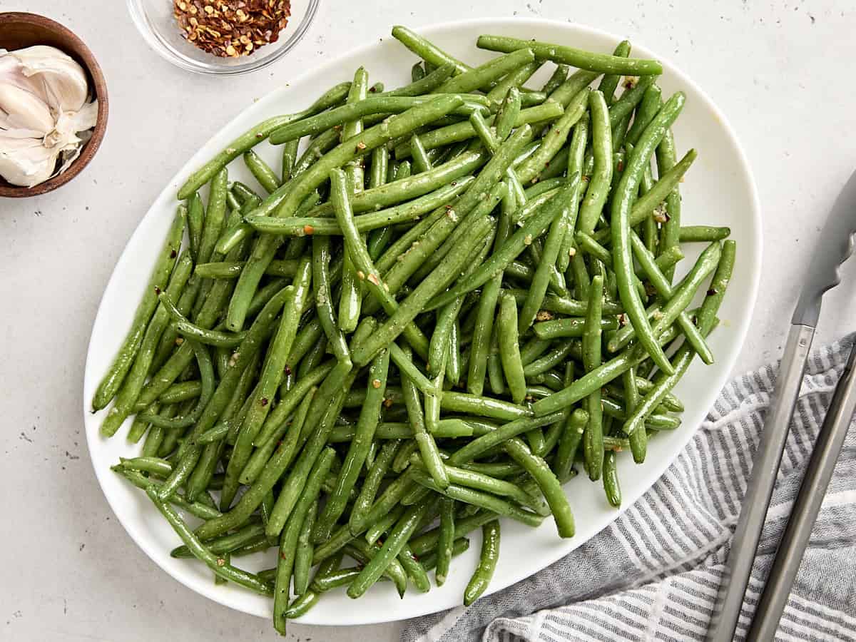 Overhead view of sauteed green beans on a white serving platter.