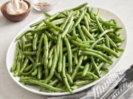 Side view of sauteed green beans on a white serving platter.