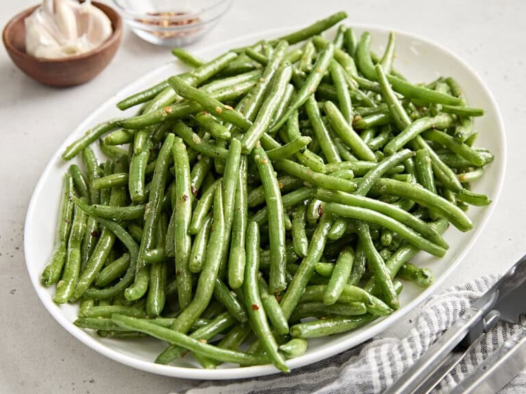 Side view of sauteed green beans on a white serving platter.