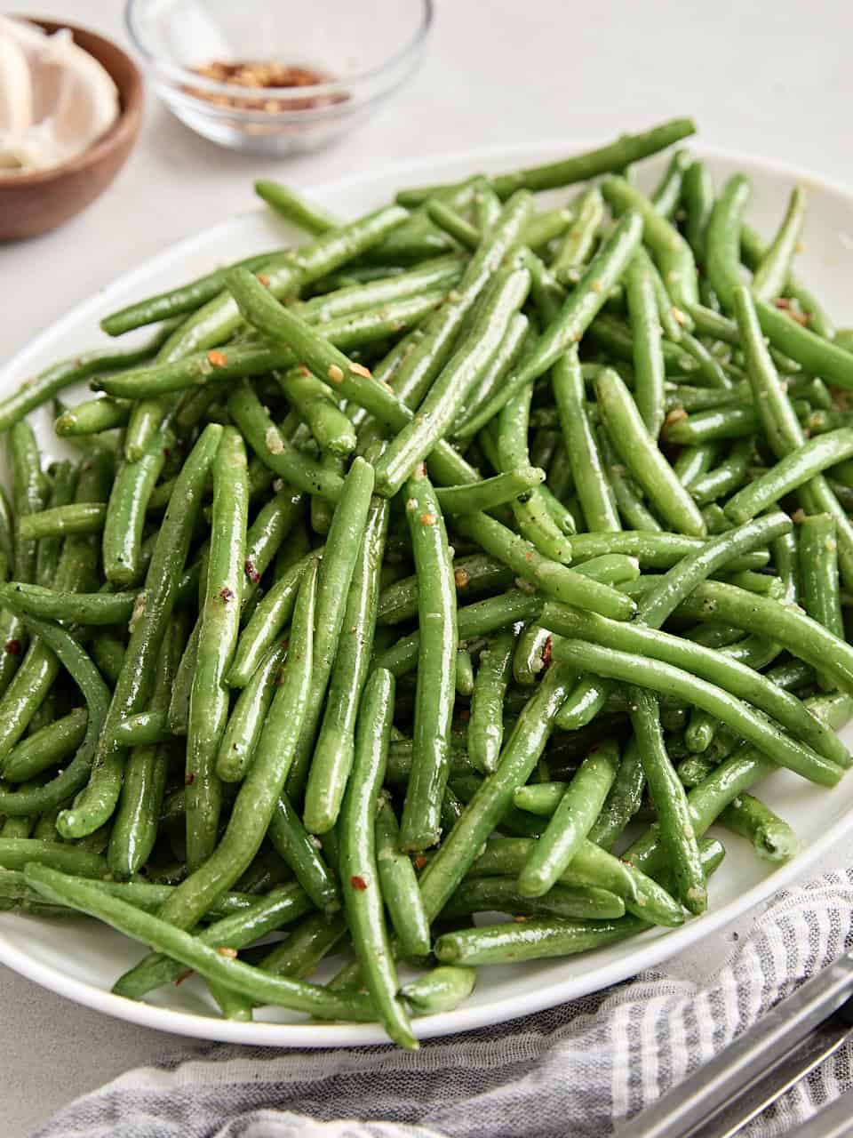 Side view of sauteed green beans on a white serving platter.