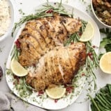 Overhead view of sliced turkey breast on a platter with fresh herbs and lemon slices as a garnish.