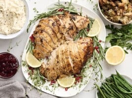 Overhead view of sliced turkey breast on a platter with fresh herbs and lemon slices as a garnish.