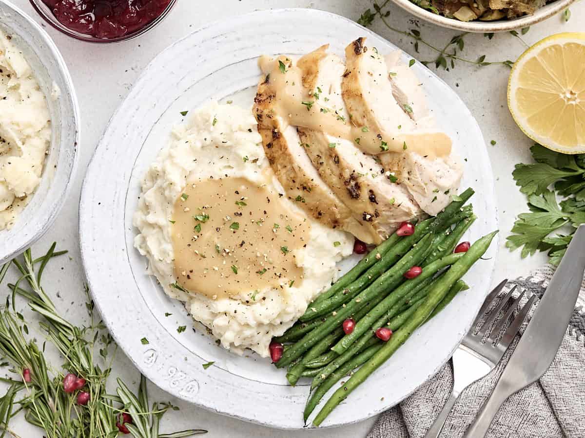 Roasted turkey breast with mashed potatoes and green beans on a serving plate.