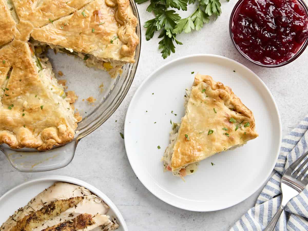 Overhead view of a slice of turkey pot pie on a plate, next to the remaining pie in a pie pan.