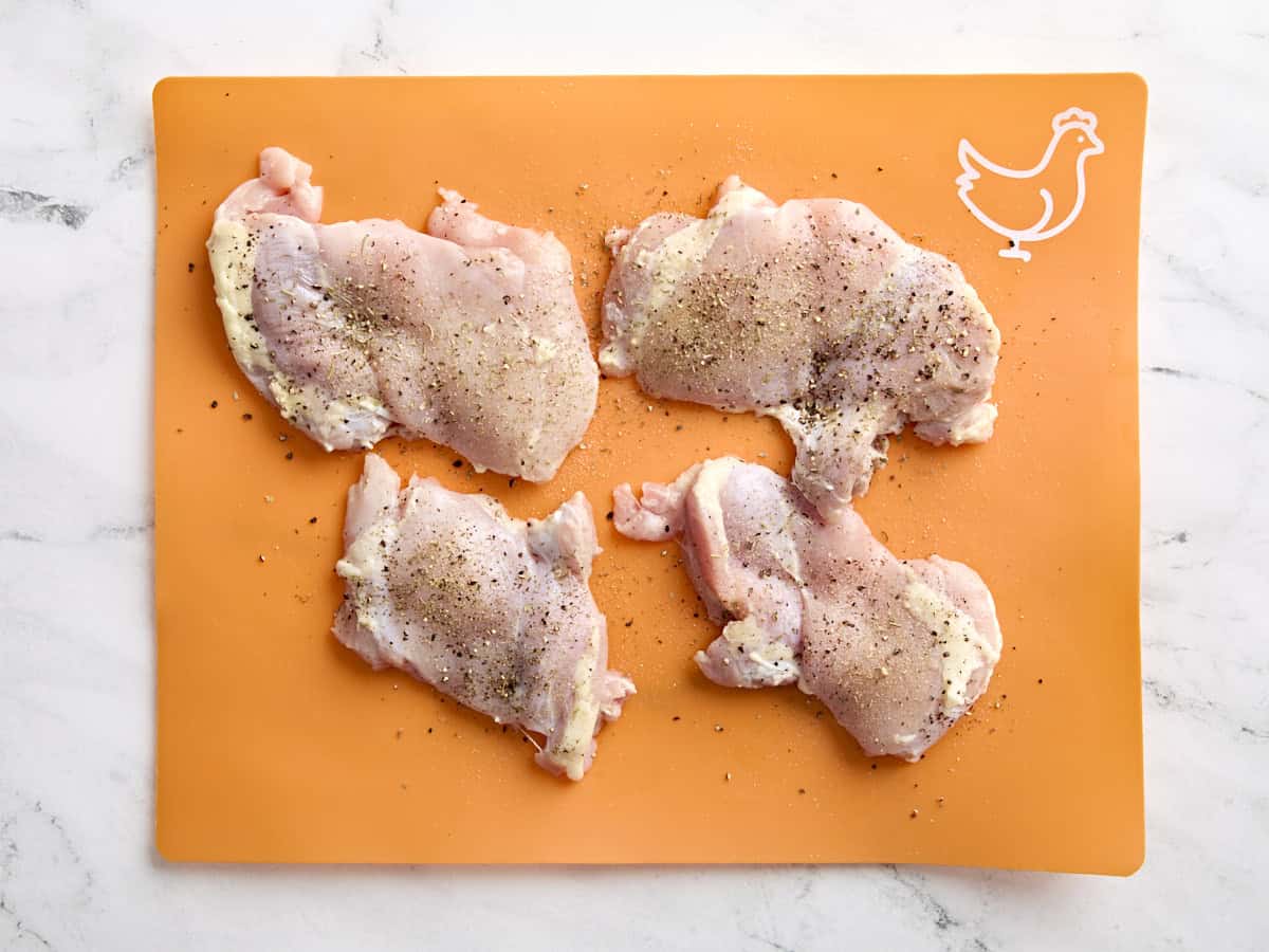 Seasoned chicken thighs on a food preparation mat.