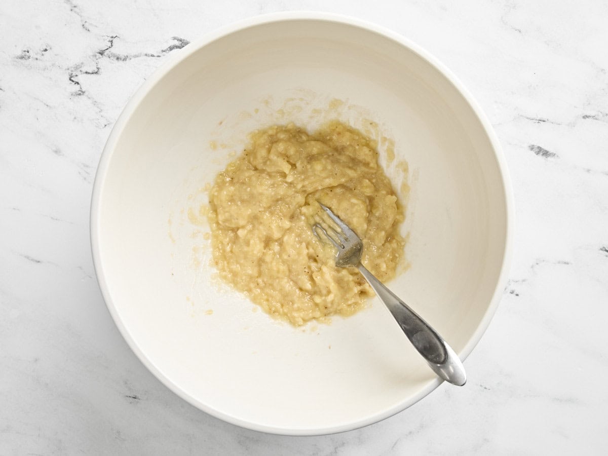 Two mashed bananas in a bowl with a fork.