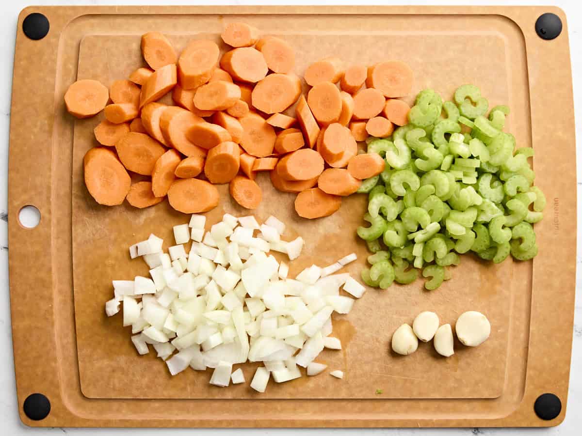 Mire poix and minced garlic cloves on a wooden cutting board.