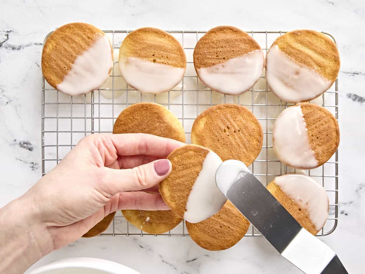 Black and white cookies being iced halfway with white icing.