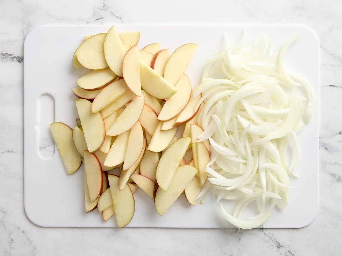 Sliced apples and onions on a white chopping board.