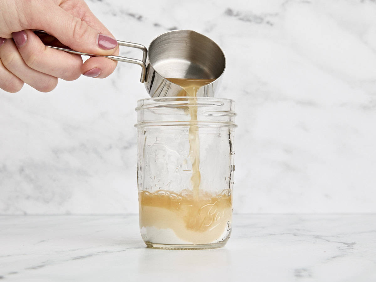 Apple cider vinegar being poured into granulated sugar in a mason jar.