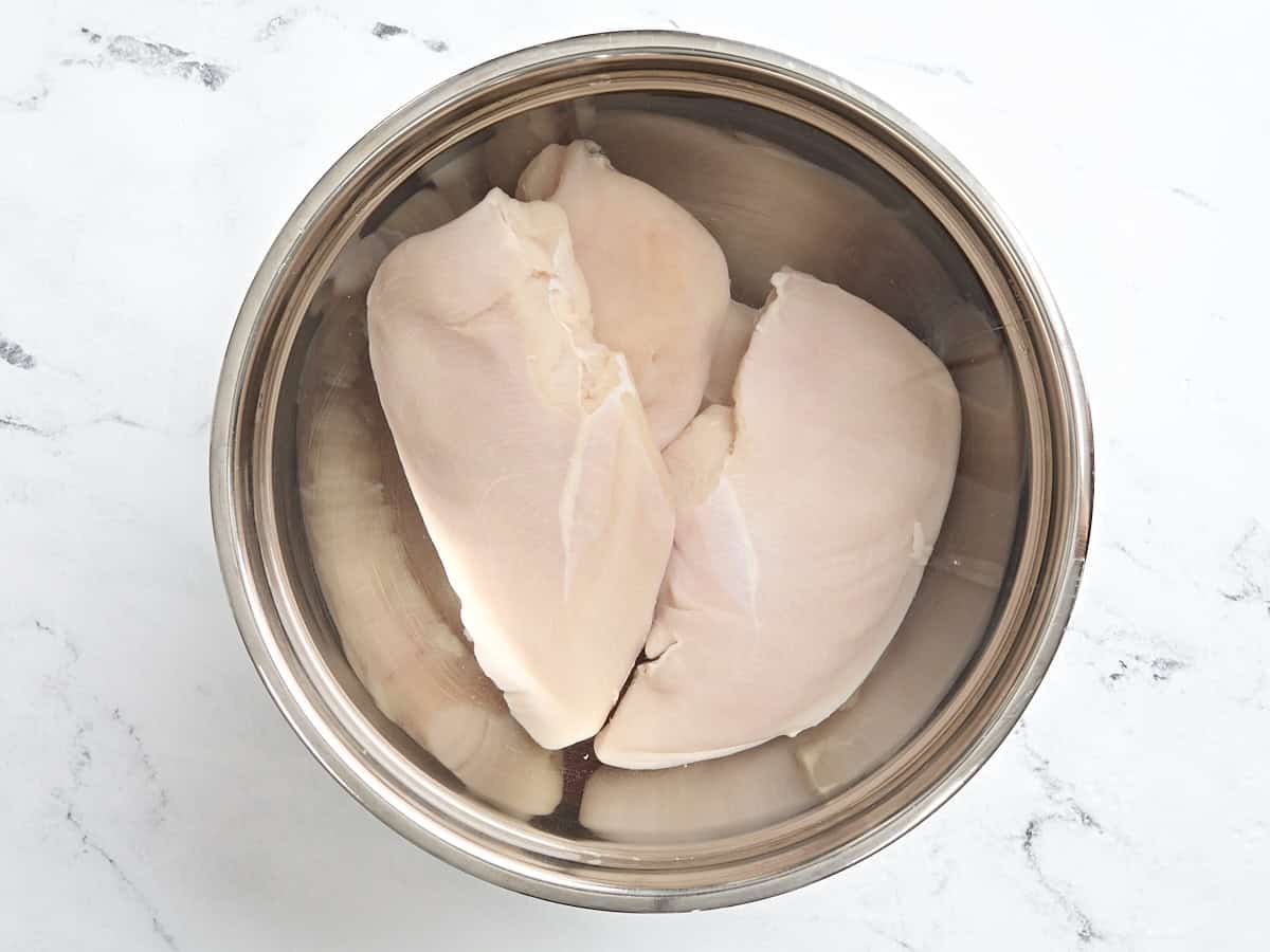 Chicken breasts brining in a bowl.