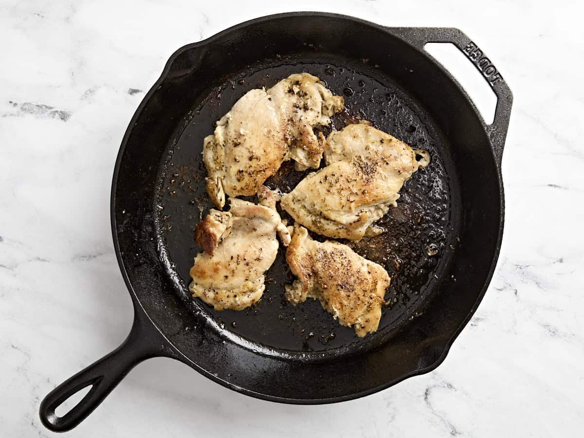 Chicken thighs cooking in a skillet.