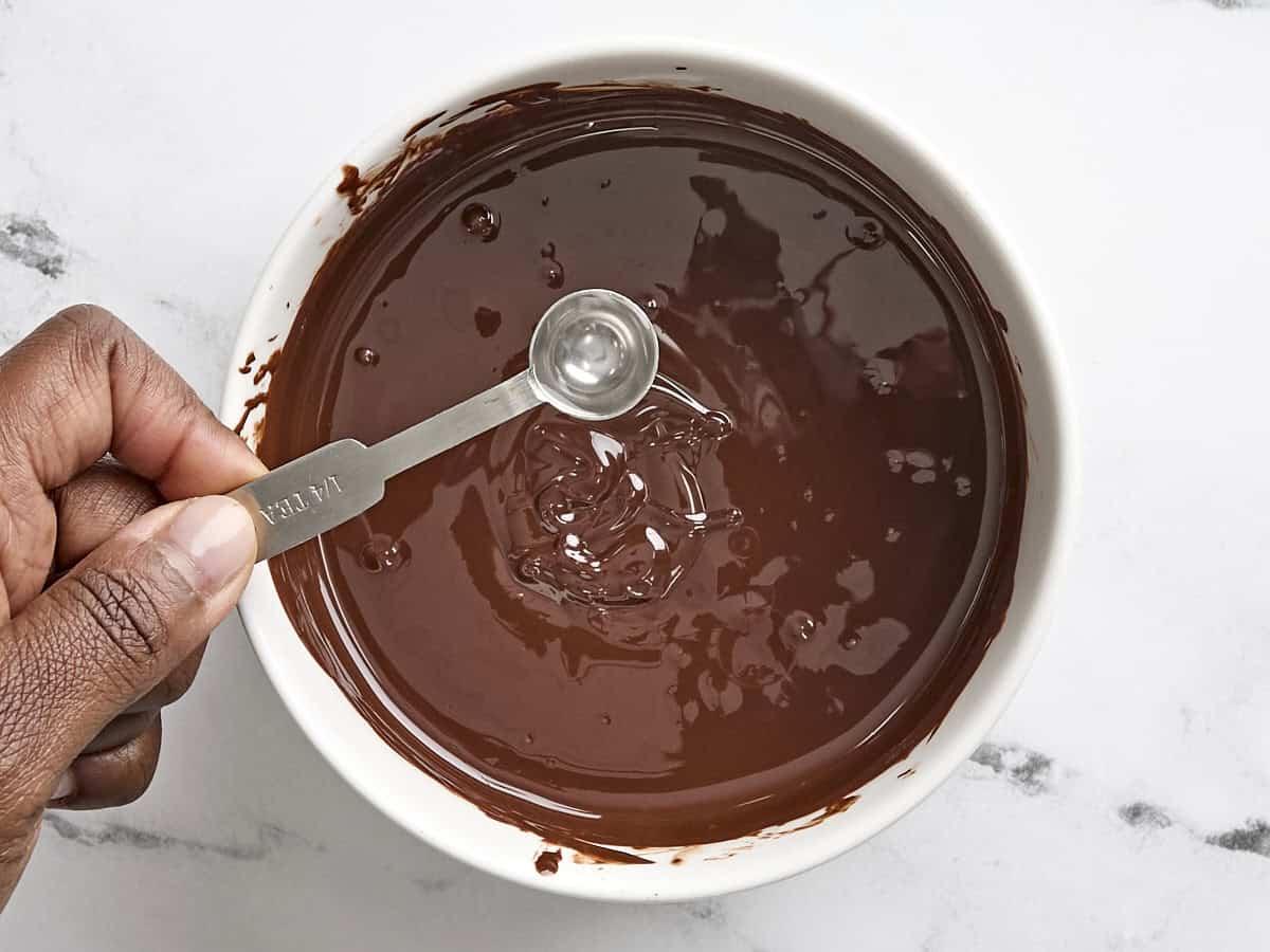 Peppermint extract being added to a bowl of melted chocolate.