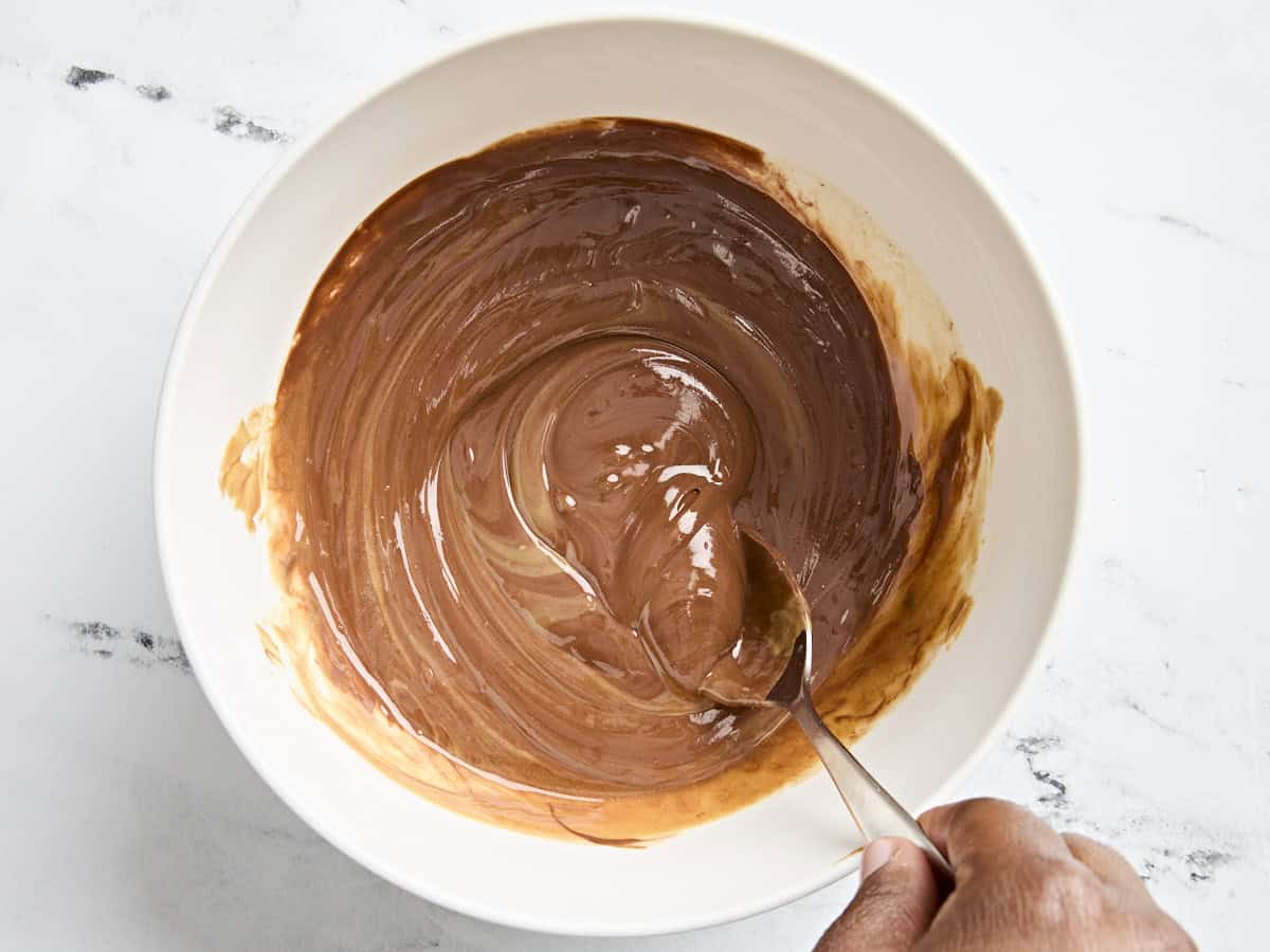 Melted chocolate and peanut butter being stirred with a spoon in a mixing bowl.