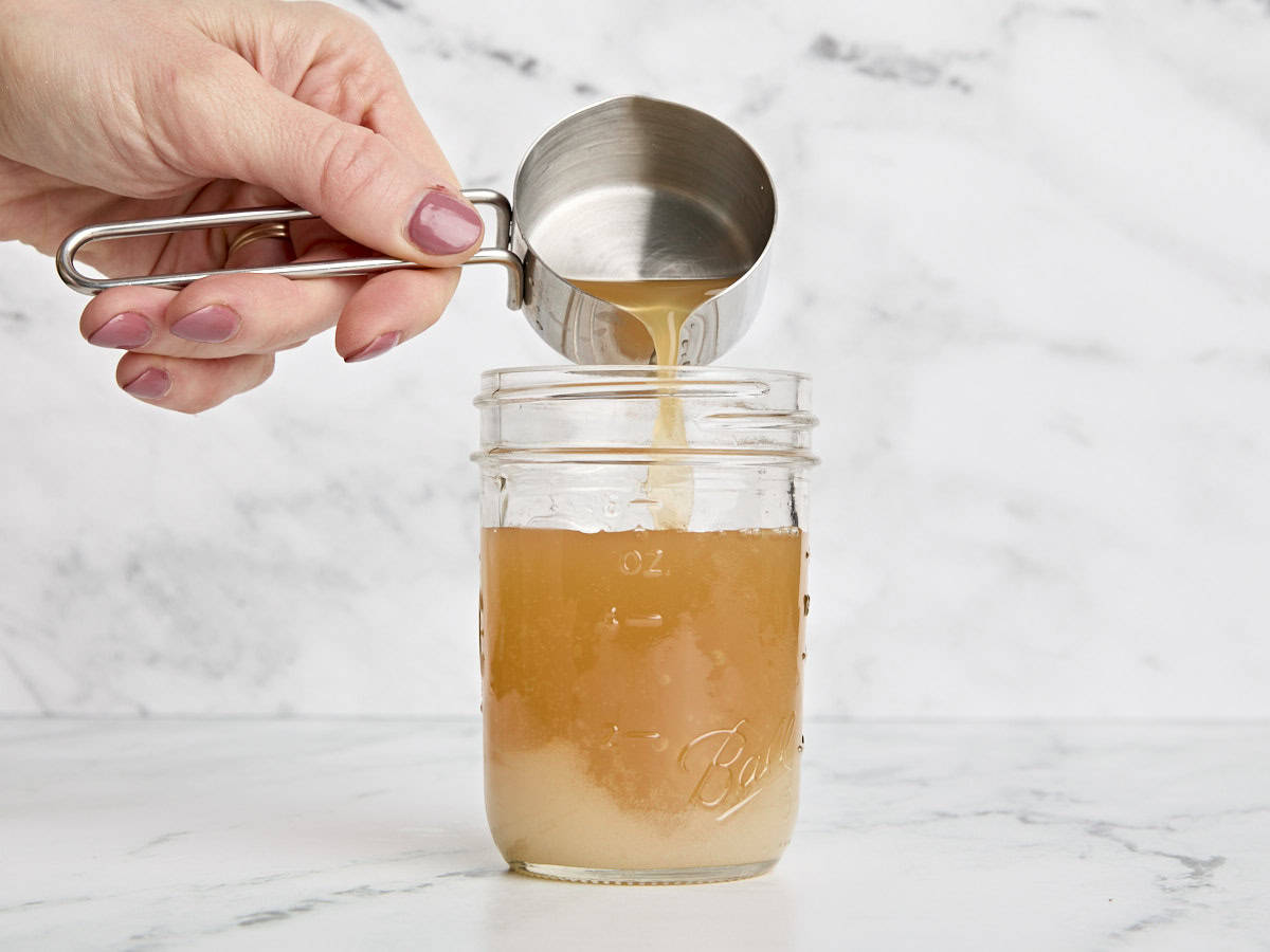 Apple cider being poured into vinegar and sugar in a mason jar.