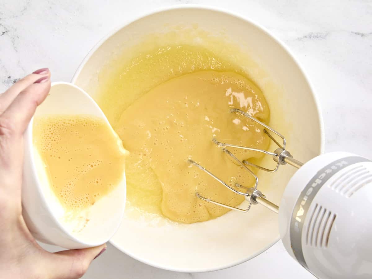 Beaten eggs being poured into melted butter and sugar mixture in a bowl.