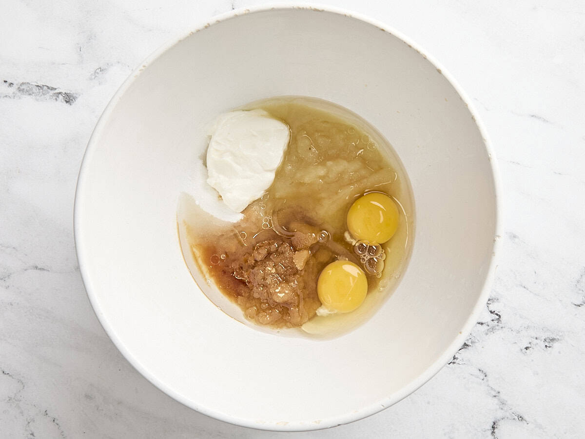 brown sugar, white sugar, yoghurt, apple sauce, oil, eggs, and vanilla in a mixing bowl.