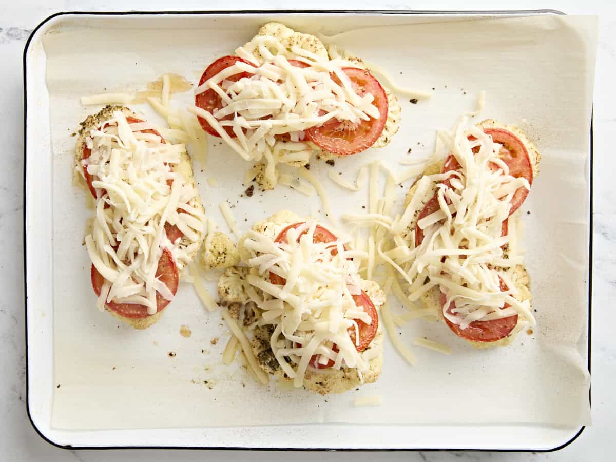 Shredded mozzarella added to cauliflower parmesan on a parchment lined baking sheet.