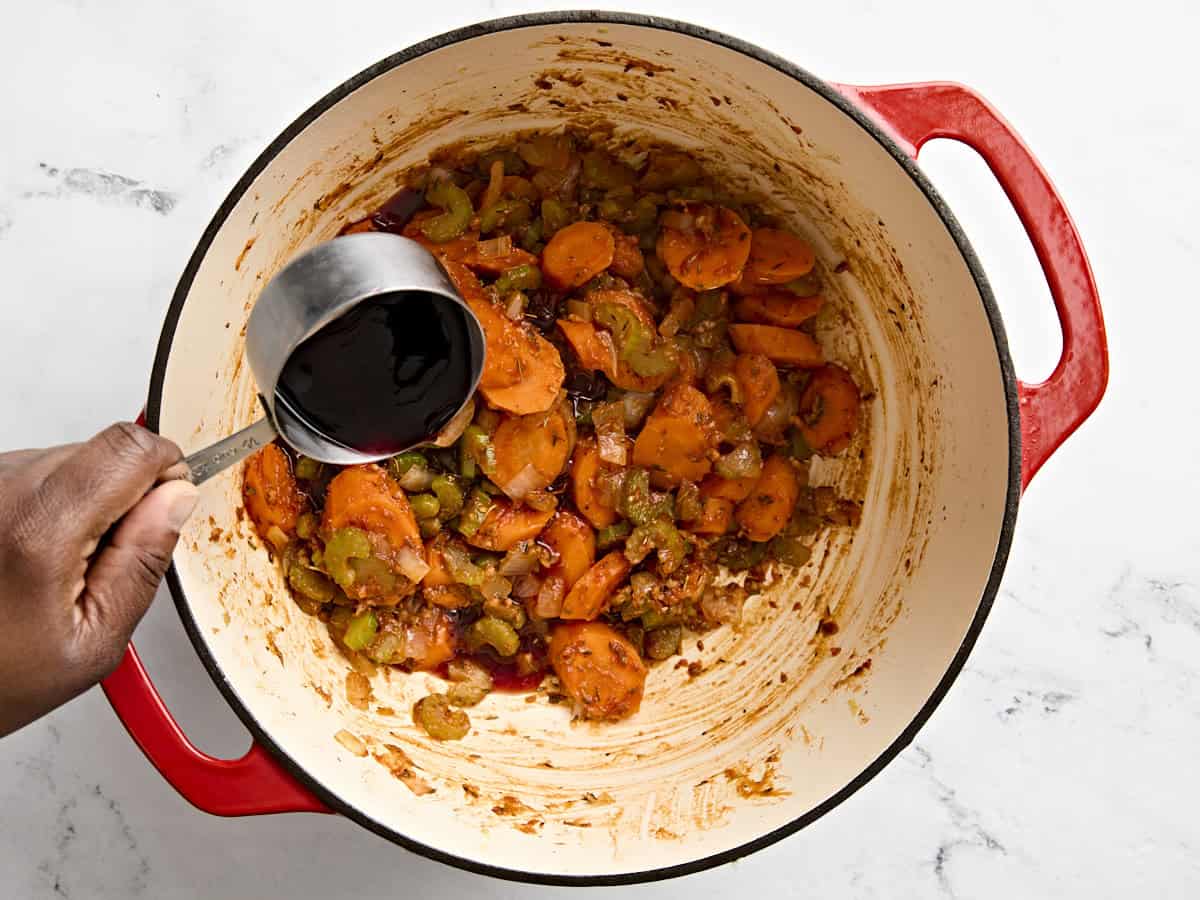 Red wine being added to beef stew in a dutch oven.