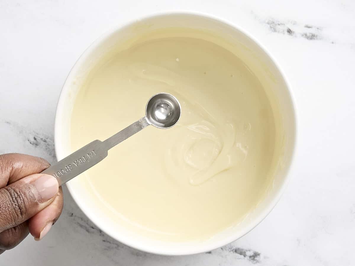 Peppermint extract being added to a bowl of melted chocolate.