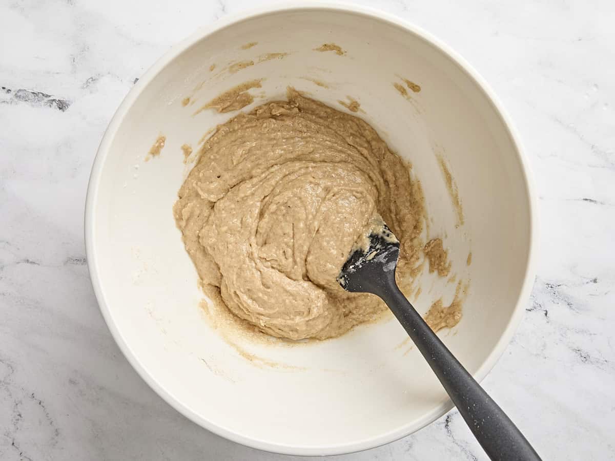 A spatula mixing apple and cinnamon muffin batter in a bowl.