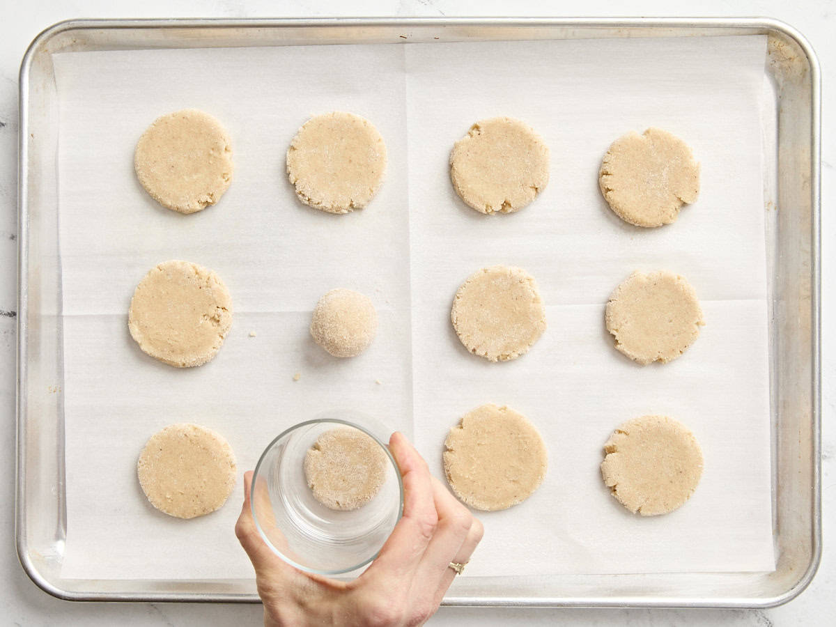 A glass flattening balls of eggnog cookie dough.