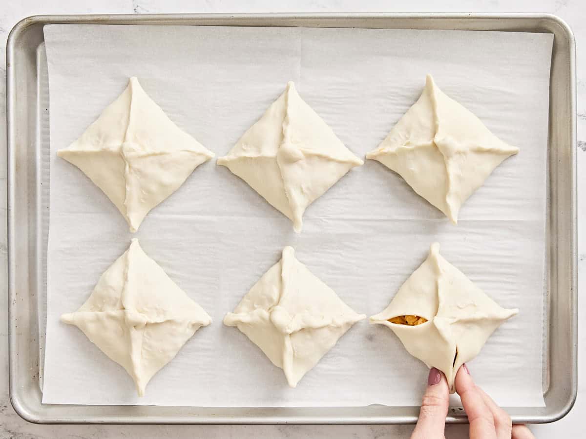 A hand pinching the edges of sausage and cheese hand pies closed.