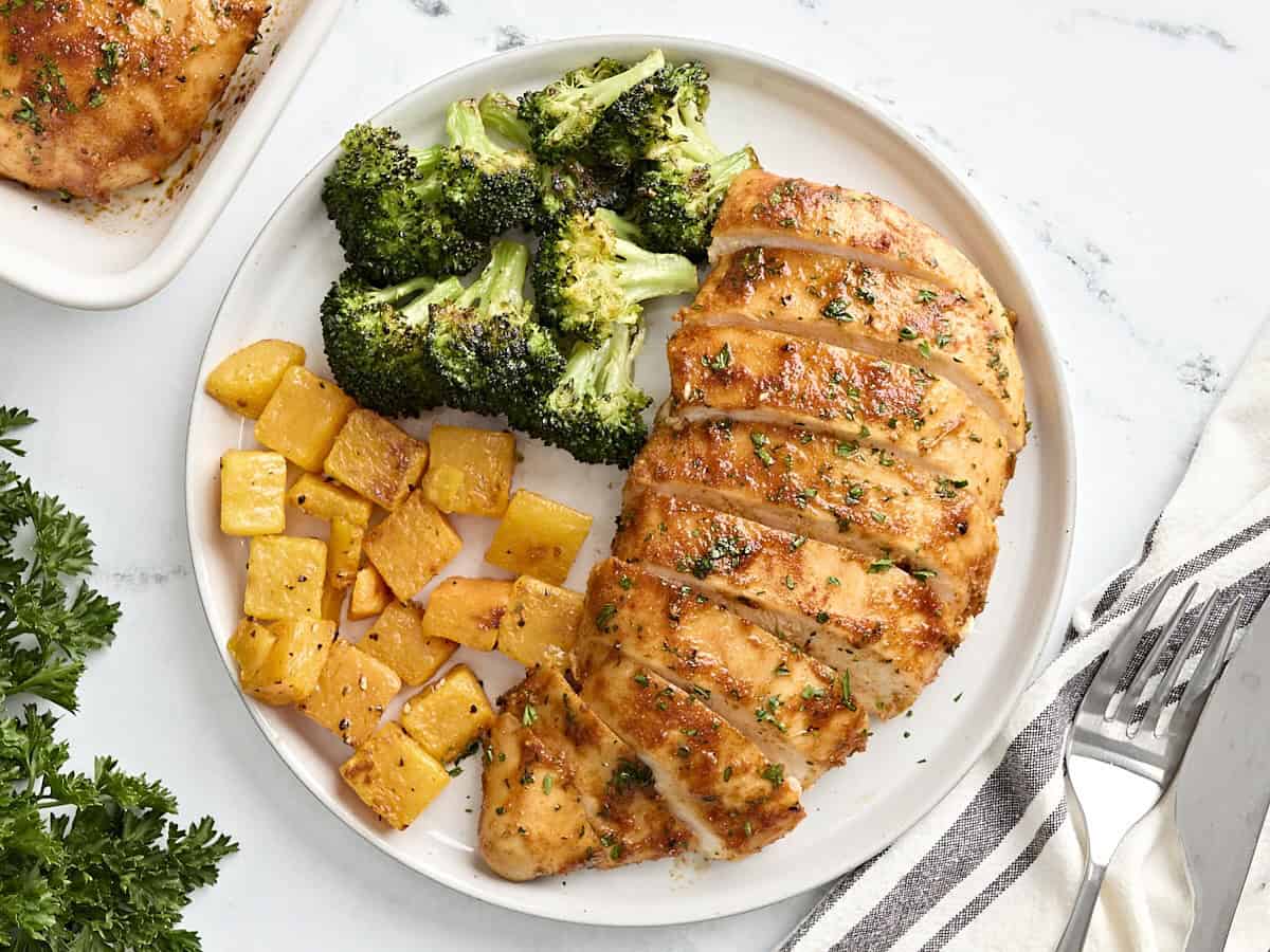 A sliced baked chicken breast on a plate with roasted broccoli and butternut squash.