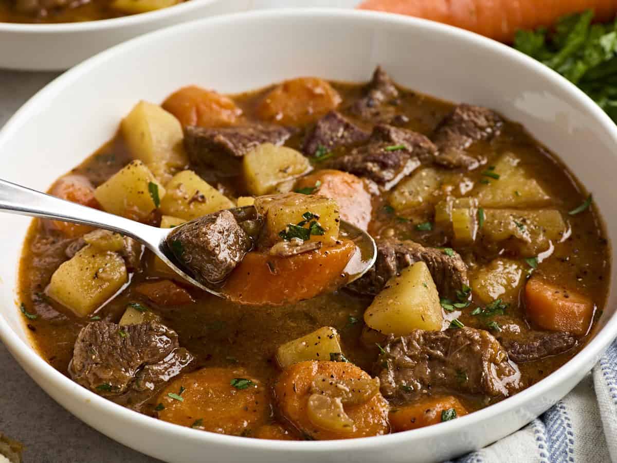 Side view of beef stew in a bowl with a spoon.