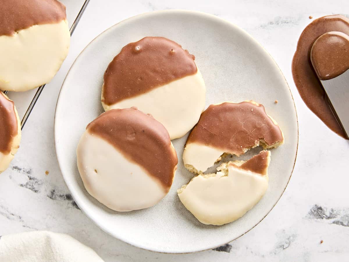 Overhead view of black and white cookies on a plate, with one broken in half.