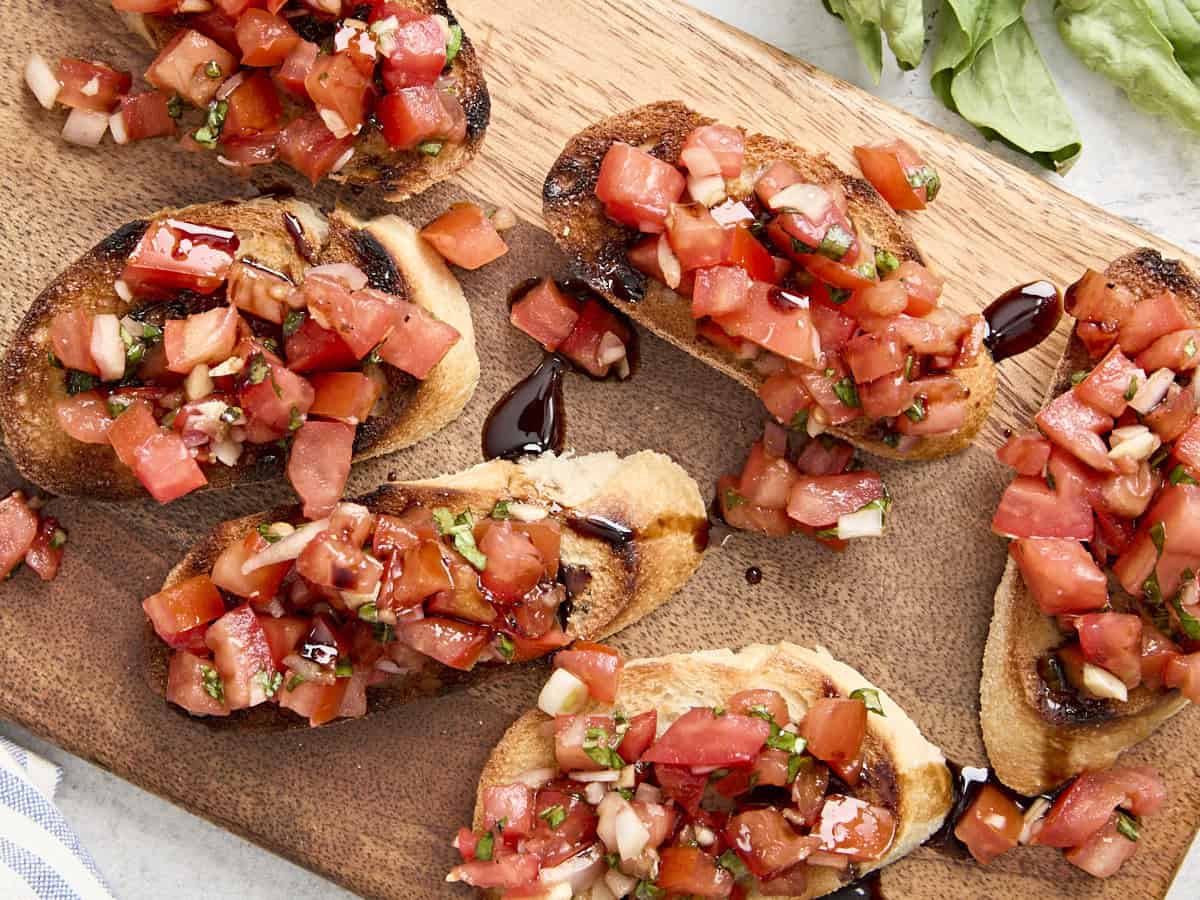 Overhead view of bruschetta on a wooden chopping board with balsamic glaze.