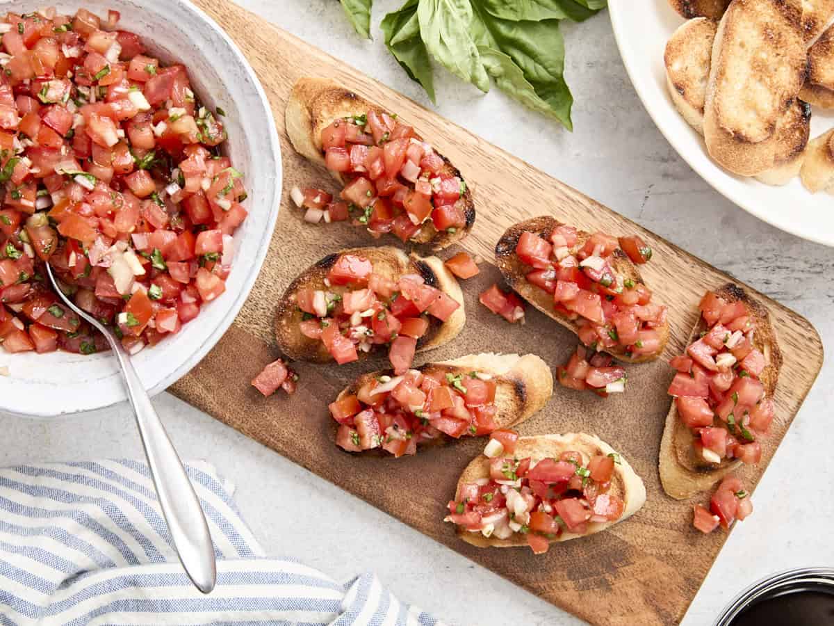 Overhead view of bruschetta on a wooden chopping board.