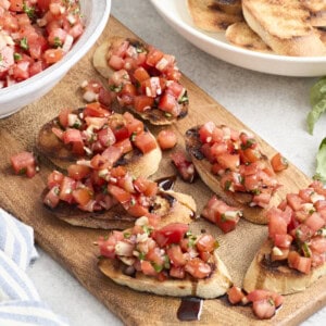 Overhead view of bruschetta on a wooden chopping board with balsamic glaze.