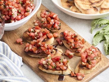 Overhead view of bruschetta on a wooden chopping board with balsamic glaze.