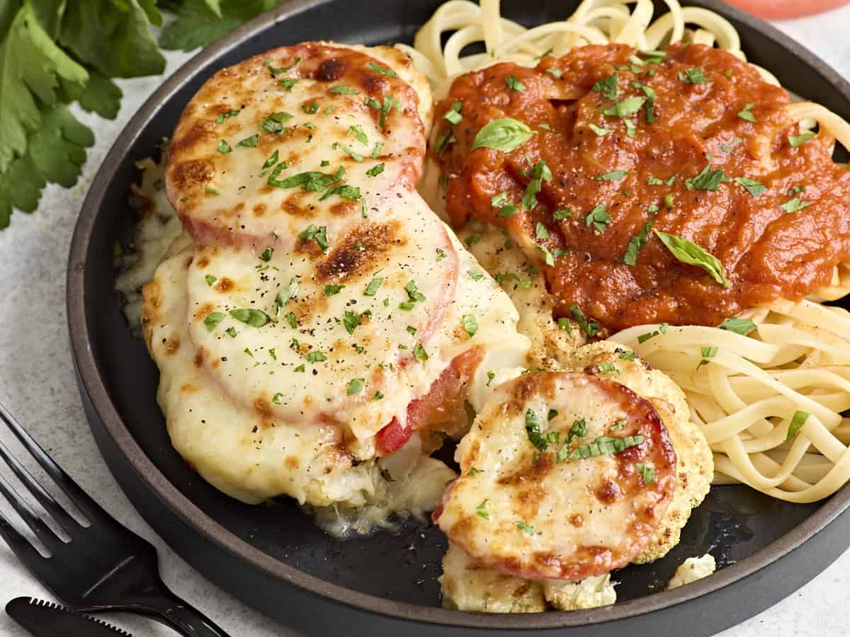 Side view of a sliced cauliflower parmesan steak on a plate with noodles and marinara sauce.