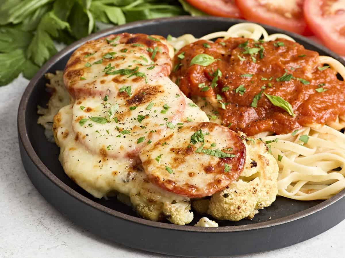 Side view of cauliflower parmesan on a plate with noodles and marinara sauce.