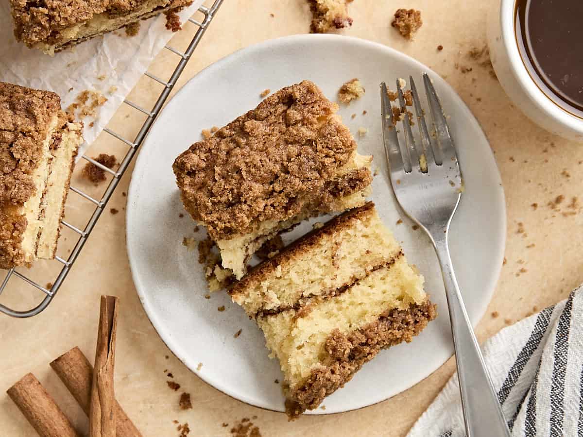 A slice of coffee cake split in half on a plate with a fork.