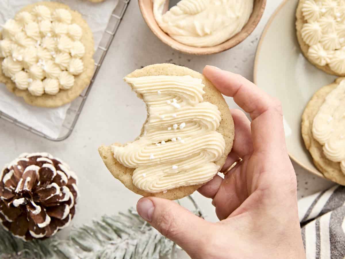 A hand holding an eggnog cookie with a bite taken out of it.