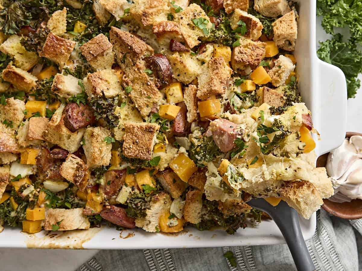 A spoon taking some savory bread pudding from a baking dish.