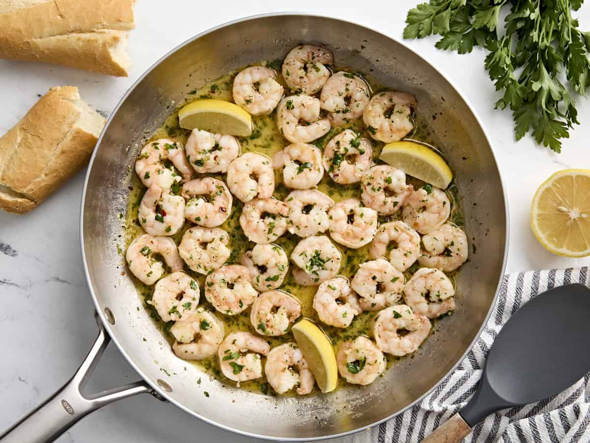 Overhead view of shrimp scampi in a skillet with lemon wedges.